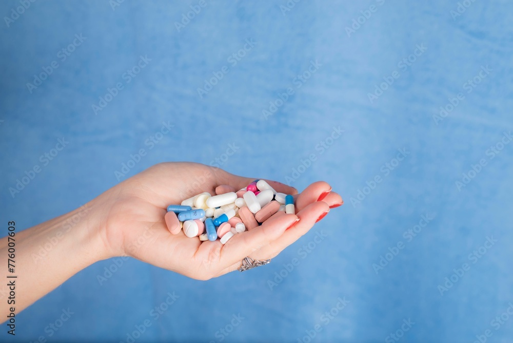 Pills in a persons palm against blue background. Medical supplies.