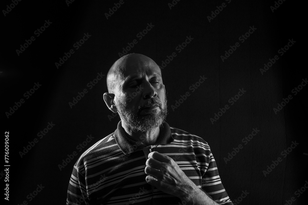 Grayscale of a handsome bald mature man with a beard wearing a casual shirt on a black background