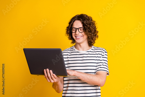 Photo portrait of handsome teenager guy hold netbook remote lesson dressed stylish striped garment isolated on yellow color background