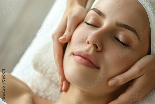Young woman getting a facial treatment in a beauty salon  in a closeup of hands applying cream on her face with her eyes closed and a towel over her head