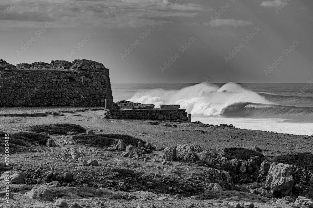Grayscale shot of the seashore with stormy waves at daytime