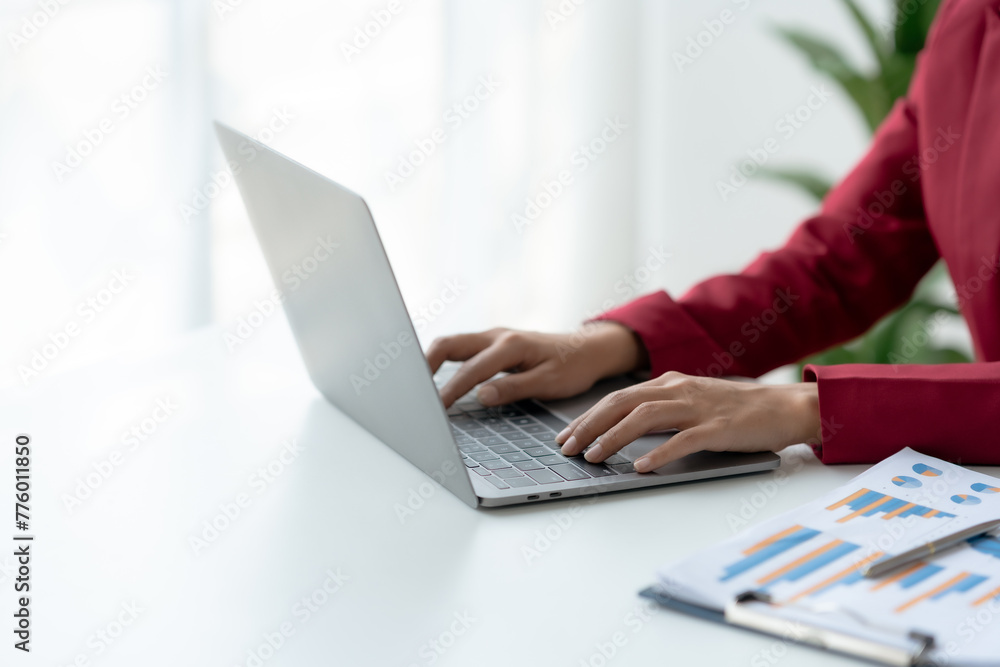 A woman is typing on a laptop in front of a plant A woman is typing on a laptop in front of a plant