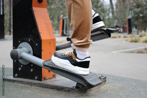 A young woman in sportswear exercising on an training apparatus outdoors in a city park.