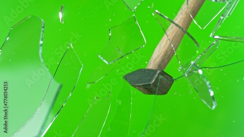 Freeze motion of glass-breaking hammer, shattering against green background