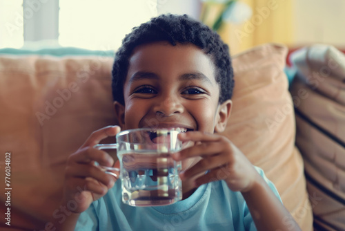 Happy African American boy with a glass of water on the sofa.