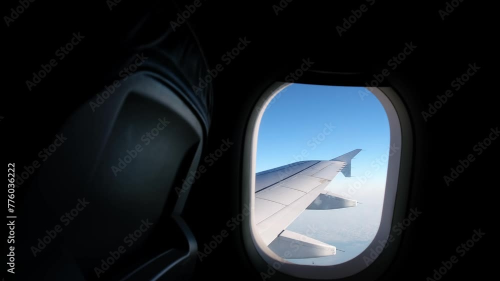 View of an airplane wing from a porthole against a blue sky background. A passenger plane flies above the clouds in the morning light. The concept of traveling by air. Fear of heights, aerophobia. 4K View of an airplane wing from a porthole against a blue sky background. A passenger plane flies above the clouds in the morning light. The concept of traveling by air. Fear of heights, aerophobia. 4K