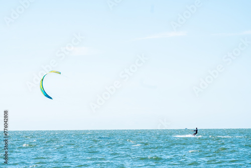 A kitesurfer harnesses the wind power, gliding across the sea's surface under a vast, clear sky. The prominent kite contrasts against the blue backdrop, adding dynamism to the serene aquatic landscape