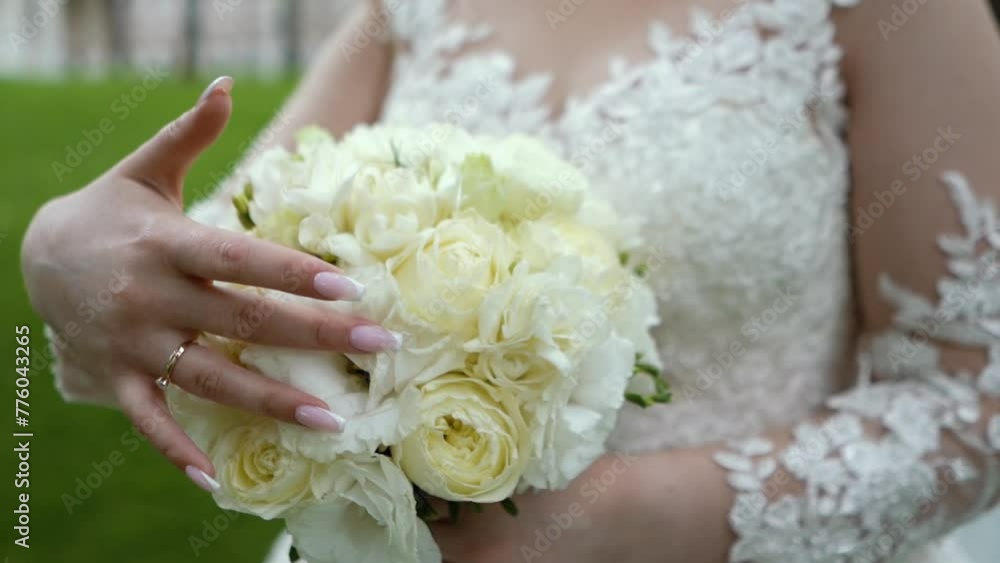 A bride with a wedding ring on her hand strokes and admires her wedding bouquet of flowers, close-up A bride with a wedding ring on her hand strokes and admires her wedding bouquet of flowers, close-up