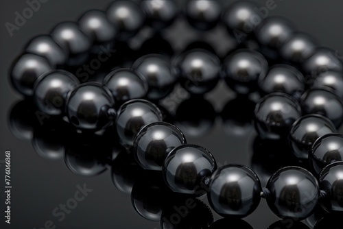 A close-up of a black pearl necklace on a dark reflective surface