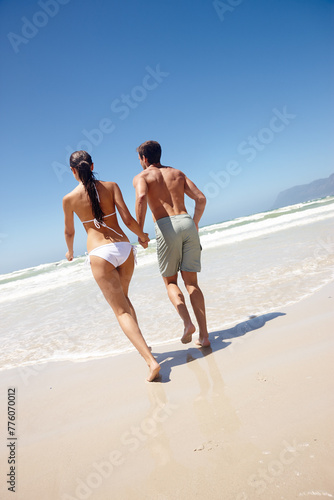 Couple, rear view and holding hands by beach with travel for bonding, summer vacation and anniversary getaway. Man, woman and love by ocean with swimwear for walking, healthy relationship or blue sky
