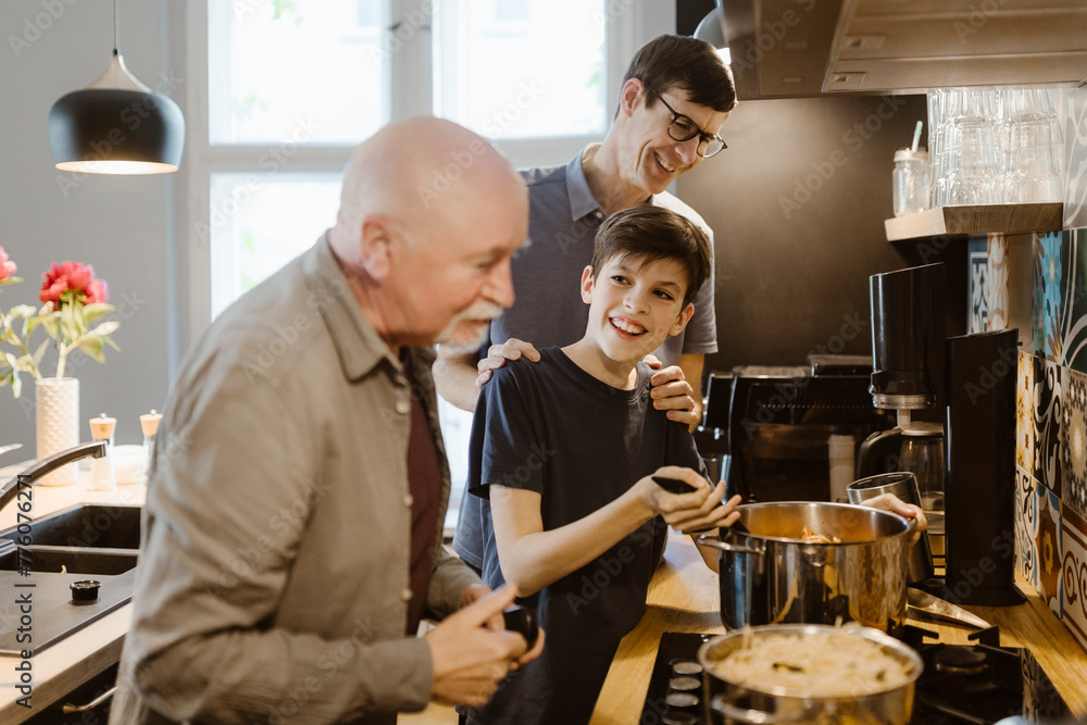 Smiling boy preparing food with grandfather and father in kitchen at home Smiling boy preparing food with grandfather and father in kitchen at home