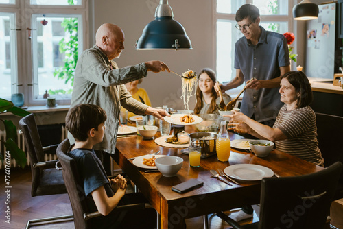 Senior man serving noodles to family while having dinner at home photo