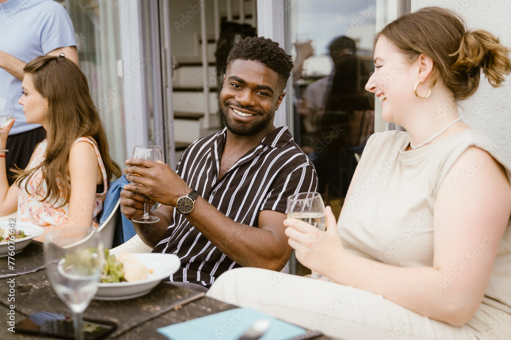 Portrait of smiling young woman having drinks with female friend sitting at dining table during dinner party in balcony Portrait of smiling young woman having drinks with female friend sitting at dining table during dinner party in balcony