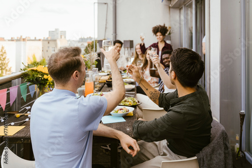 Men toasting drinks with group of friends sitting at dining table in balcony photo