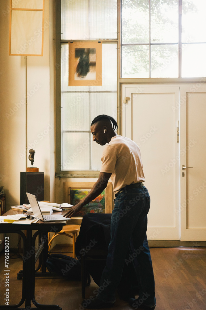 Side view of male entrepreneur using laptop while standing in home office Side view of male entrepreneur using laptop while standing in home office
