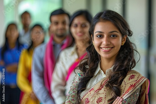 A poised Indian businesswoman smiles confidently in professional attire with her multicultural team blurred in the background.