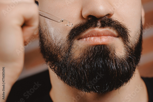 Barber applies for growth beard oil with dropper for man in barbershop. Concept spa cosmetic and treatment wellness and natural beauty of skin men