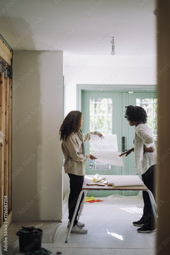 Female design professional discussing with customer while standing in under construction apartment Female design professional discussing with customer while standing in under construction apartment