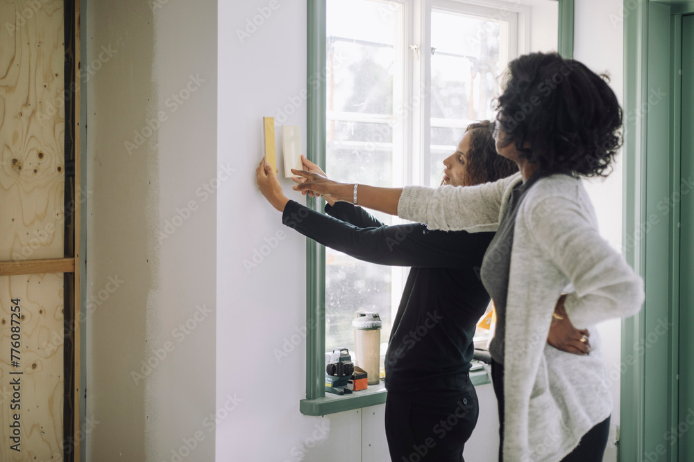 Female customer and architect choosing wall paint color while standing near window at under construction apartment Female customer and architect choosing wall paint color while standing near window at under construction apartment