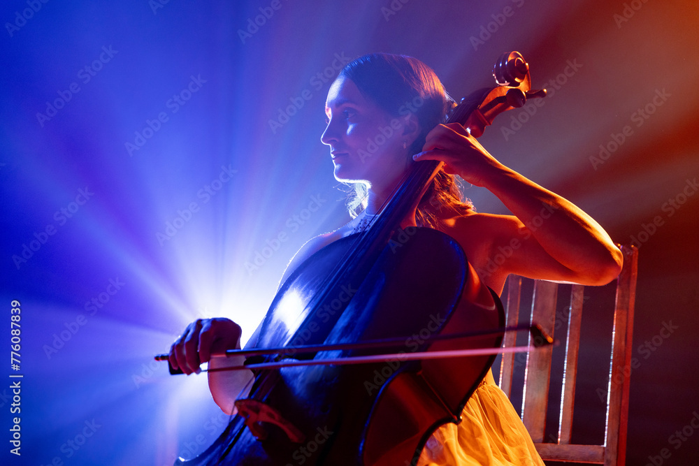 Fototapeta premium Cellist immersed in music, with striking halo of stage lights accentuating her silhouette on stage. Classic music in modern life. Concept of hobby and work, music festivals, concerts, symphony show.