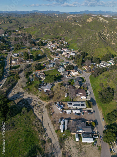 Val Verde, California - an unincorporated community located in northwestern Los Angeles County - is shown from an aerial, vertical view, with homes and the surrounding, green mountains visible.
