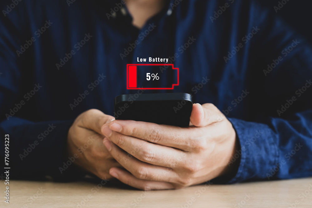 Concept of low battery, technology and reserve energy. Hand using smart phone with low battery sign warning in the office - obrazy, fototapety, plakaty 