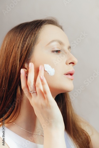 Beautiful young woman applying cream on the cheek. Face Skin care concept