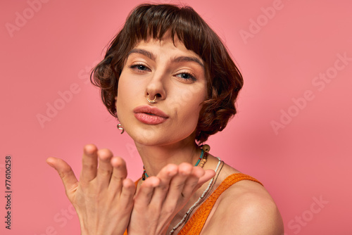 Foto flirty young woman with nose piercing and short brunette hair sending air kiss o