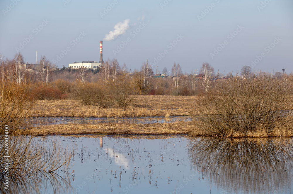 Pipes of a power station reflected in water against a blue sky