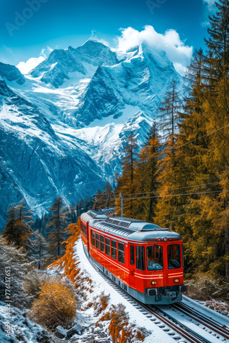 Red train is going through snowy mountain landscape with evergreen trees in the background and large mountain in the distance. © valentyn640