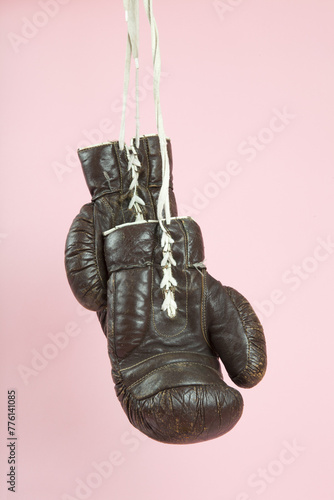 a pair of old boxing gloves hung in front of a candy-pink background