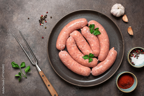 Homemade raw sausages in a plate on a dark grunge background. Top view, flat lay.
