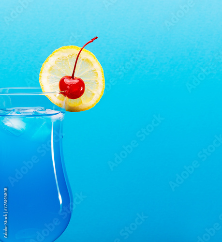 Close up of blue lagoon cocktail garnished with a slice of lemon and cherry isolated on turquoise background with space for text.