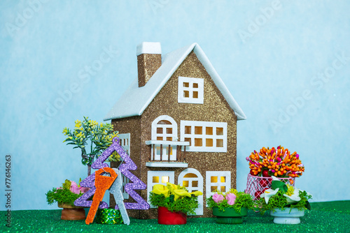 On a light blue background, a brown house with keys on a Christmas tree and many flowers around