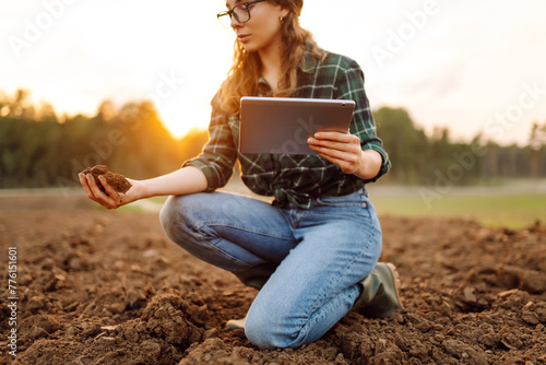Farmer woman with a digital tablet holds black soil in her hands and checks the quality. Concept of technology, ecology and gardening. © maxbelchenko