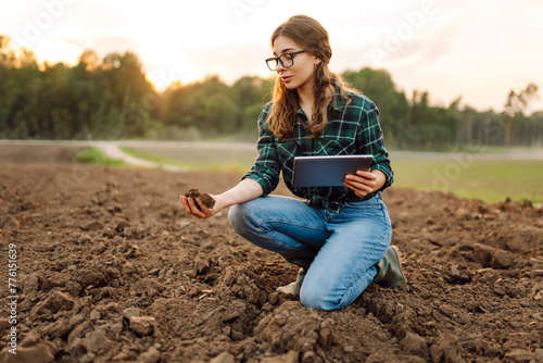 Farmer woman with a digital tablet holds black soil in her hands and checks the quality. Concept of technology, ecology and gardening.