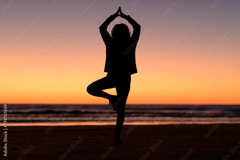 Woman silhouette doing yoga postures at the beach before sunrise