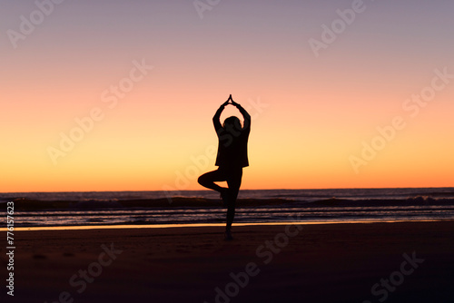 Woman silhouette doing yoga postures at the beach before sunrise