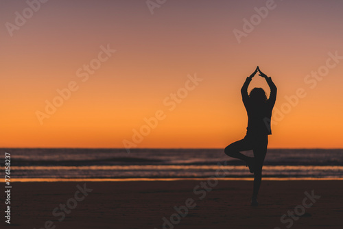 Woman silhouette doing yoga postures at the beach before sunrise © Charles Riesco