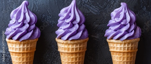   Three ice cream cones, each topped with purple icing, against a black surface and backdrop of a black wall