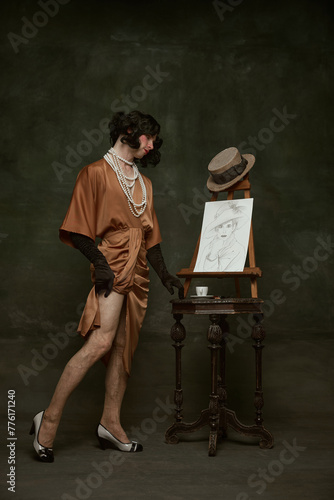 Obraz na plátně Full-length portrait of man dressed as woman in old-fashion silky dress and reaching to table with cup of coffee and self portrait in vintage room