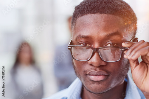 a black man in a blue shirt adjusts his glasses.