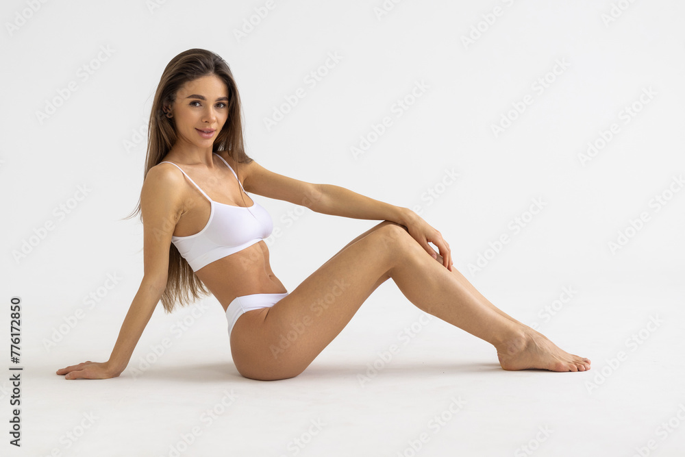 One young beautiful tanned woman with perfect figure in grey underwear lying on floor over background.