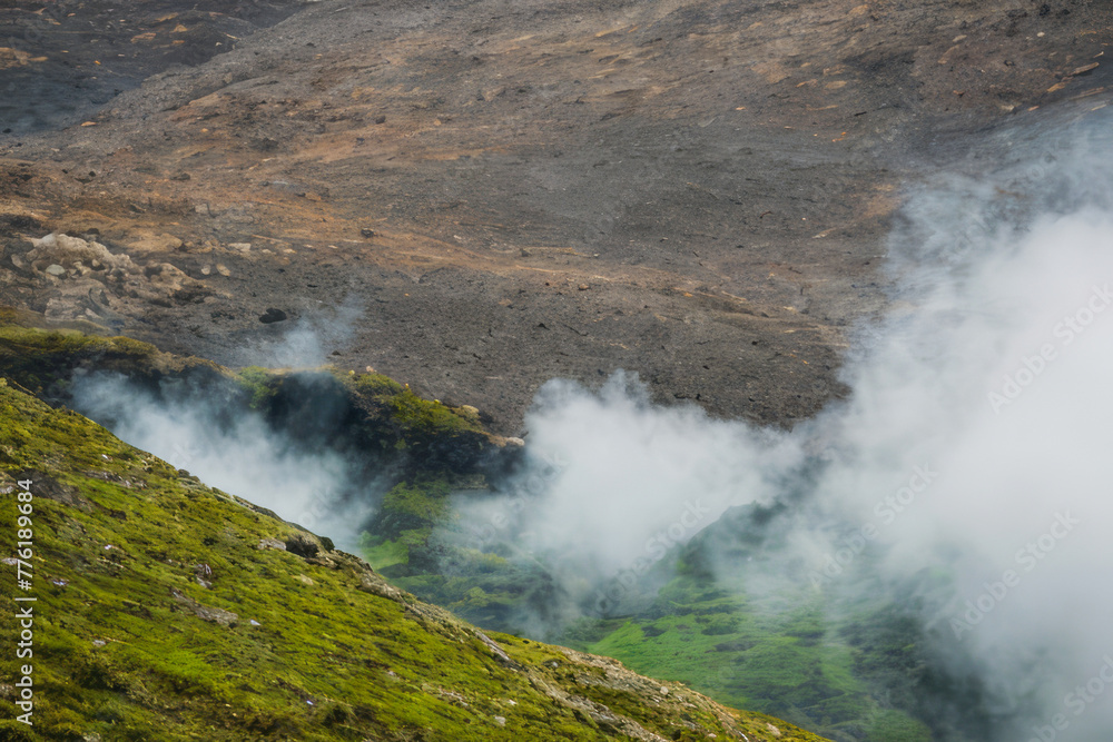 Obraz premium A cascading waterfall plunges down moss-covered mountains in a geothermal landscape
