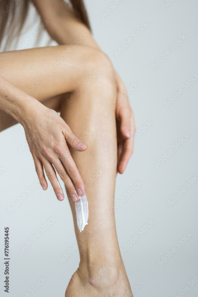 Young woman applying body cream onto hip on light grey background, closeup Young woman applying body cream onto hip on light grey background, closeup