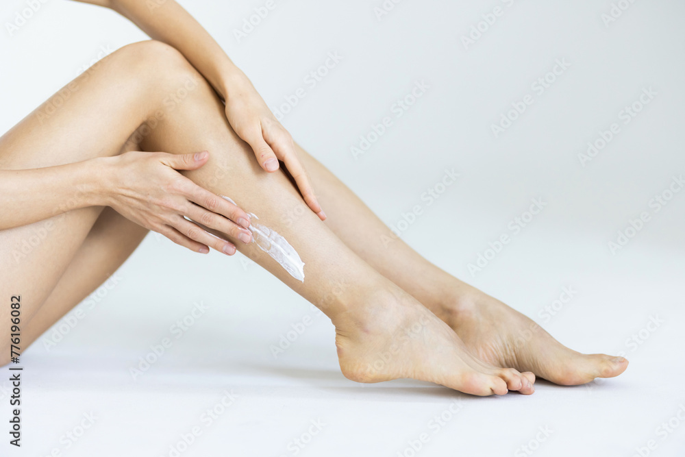 Woman applying body cream onto her smooth legs on light grey background Woman applying body cream onto her smooth legs on light grey background