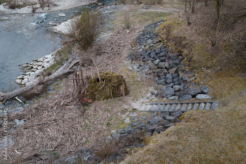 Primitive Holzhütte am Wasser gebaut aus Treibholz und Moos direkt unter Staumauer