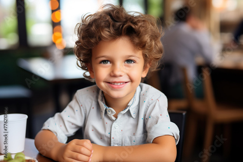 Portrait of smiling little boy sitting at table in cafe and looking at camera