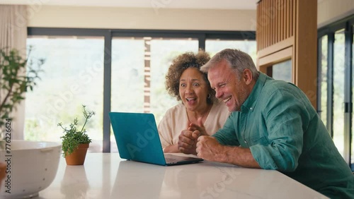 Multi-racial mature couple at home celebrating good mews looking at laptop together- shot in slow motion photo