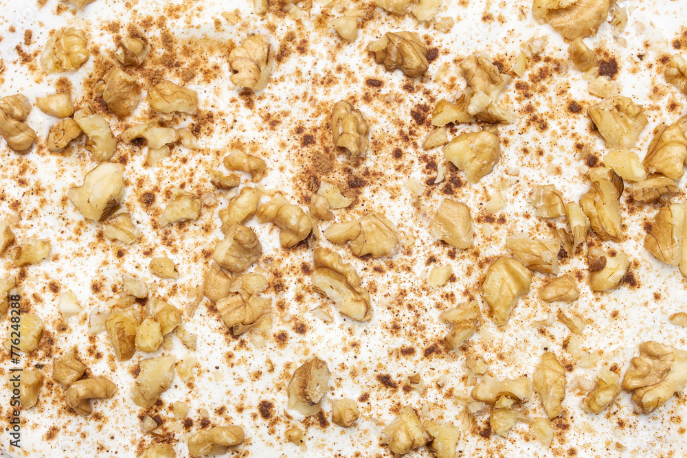 Scattered walnut pieces and sprinkled cinnamon create a dynamic contrast on a pristine white chipped cream cheese background in this home made carrot cake. Organic abstract background. Scattered walnut pieces and sprinkled cinnamon create a dynamic contrast on a pristine white chipped cream cheese background in this home made carrot cake. Organic abstract background.
